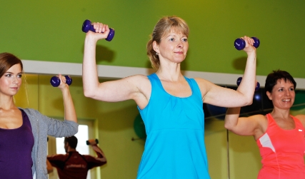 Sporterlinen stehen im Kurssraum und trainieren ihre Arme mit Handeln